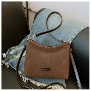 Detail der braunen Wildleder-Tragetasche mit Markenplakette auf Denim-Hintergrund