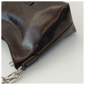 Detail der dunkelbraunen glänzenden Ledertasche mit silbernen Beschlägen und feinen Nähten