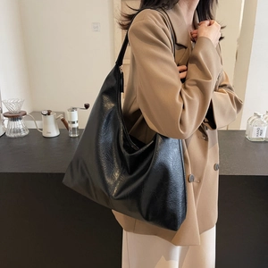 Large black leather tote bag with vintage texture worn by model in a cozy cafe