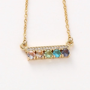 Close-up of gold chain necklace with colorful gemstones and white zircon bar pendant