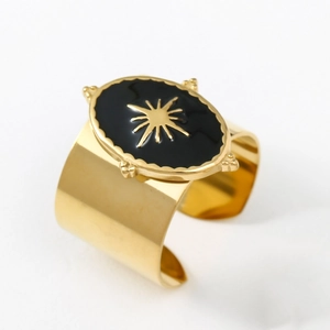 Close-up of golden wide cuff bracelet with oval black inlay and starburst engraving