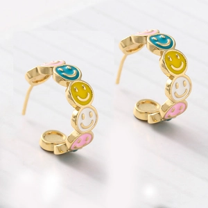 Detailed close-up of C-shaped gold hoop earrings featuring colorful enamel smiley faces