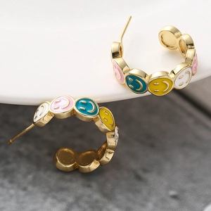 Macro shot of gold C-shaped earrings with colorful enamel smiley face patterns