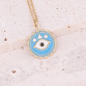 Macro detail of gold evil eye pendant with blue enamel on a natural stone background