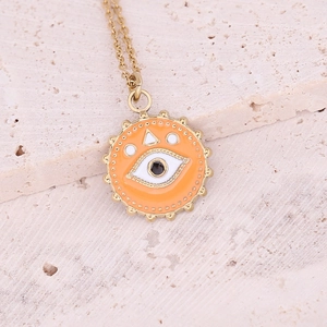 Close-up of golden evil eye pendant with orange enamel on a textured stone surface