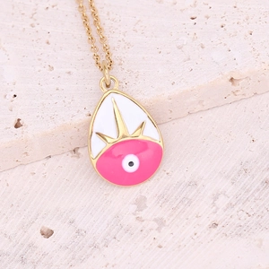 Macro shot of gold teardrop evil eye pendant with pink enamel detail on stone surface