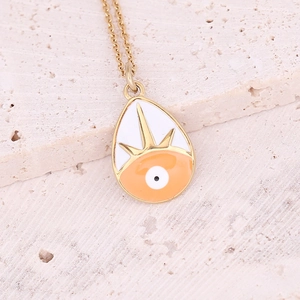 Macro shot of a teardrop evil eye pendant with orange enamel and gold chain details