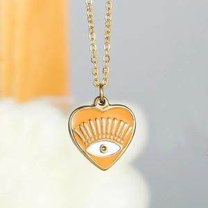 Macro detail of 14k gold plated heart pendant with orange enamel and evil eye motif
