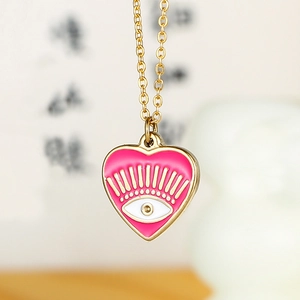 Macro detail of a 14k gold plated heart pendant with pink enamel and evil eye motif