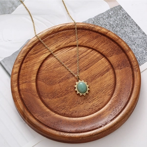 Detailed close-up of a vintage sunflower necklace with a green oval gemstone on a wooden tray