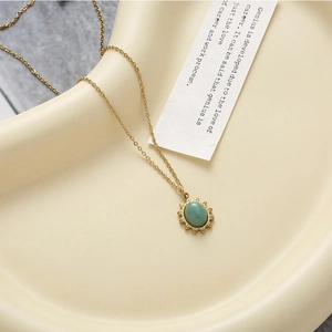Detailed shot of a green stone pendant on a gold chain over a ceramic plate