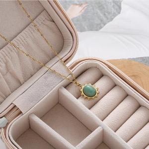 Vintage gold necklace with green gemstone pendant on soft pink jewelry organizer