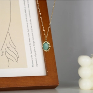 Detail of vintage gold necklace featuring an oval green gemstone pendant on a wooden frame