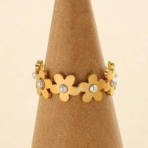 Minimalist gold flower ring with pearl centers on a wooden stand for an elegant display