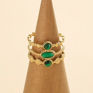 Detailed macro of gold stacked rings with green stones on a wooden jewelry display stand