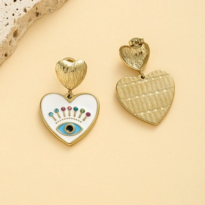 Macro detail of gold heart earrings with white enamel evil eye and rhinestone inlay