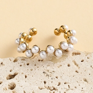 Gros plan d'une bague dorée ondulée sertie de perles rondes sur un support en pierre
