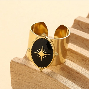 Adjustable wide gold ring with black enamel and gold starburst pattern on wooden stand