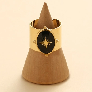 Golden wide band ring with black enamel and star motif on a wooden display stand