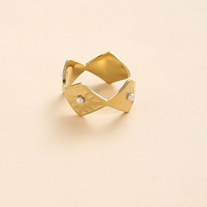 Gros plan sur une bague géométrique dorée avec perles blanches et détails gravés