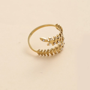 Detailed macro view of golden leaf ring with zircon stones on beige background