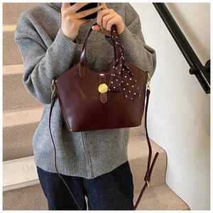 Sac fourre-tout bordeaux mat avec boucle dorée et foulard à pois sur un mannequin
