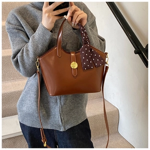 Sac seau en cuir marron avec foulard en soie et boucle dorée sur un décor d'escalier
