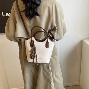 Elegante bolso de hombro crema con asas marrones y correa sobre una gabardina color caqui