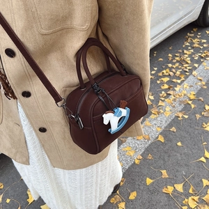 Matte dark brown bowling handbag with horse charm shown on autumn street outfit