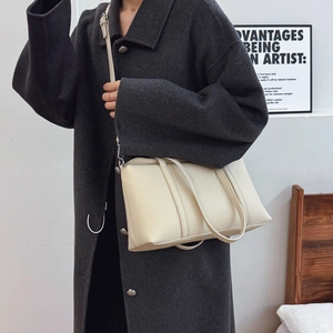 Minimalist beige leather tote bag with crossbody strap shown on grey coat model