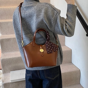 Sac seau en cuir marron avec foulard à pois et boucle dorée porté par un modèle