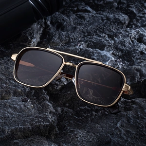 Lunettes de soleil aviateur carrées pour hommes avec monture dorée sur roche volcanique