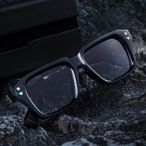 Square dark blue sunglasses with gold rivets on a black rock surface