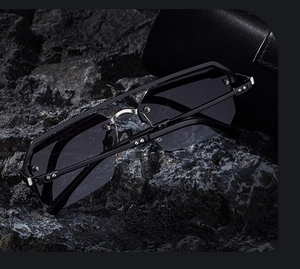 Détail de lunettes de soleil carrées sans monture avec pont argenté sur roche noire