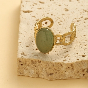 Golden textured open ring for women featuring an oval green gemstone on stone background