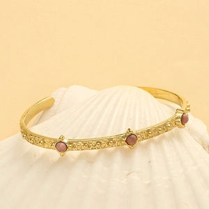 Detailed close-up of a gold-plated vintage cuff bracelet with pink stones on a white shell