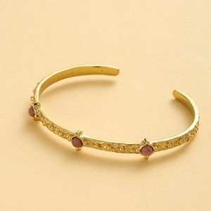 Detail of hammered gold cuff bracelet featuring three round pink natural stone inlays