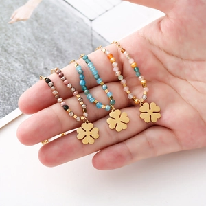 Three beaded clover necklaces with gold pendants held in hand over a magazine background