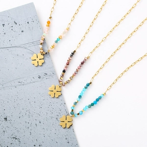 Three gold clover necklaces with colorful beads on a modern textured background