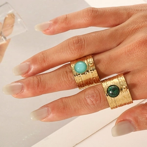 Wide gold stainless steel rings with natural blue and green stones on model hand