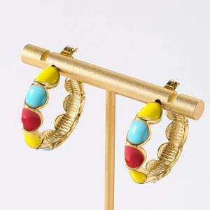 Close-up of golden C-shaped hoop earrings with colorful enamel and scallop edges