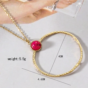 Macro shot of gold hammer textured ring pendant with red stone on a delicate chain