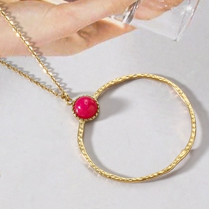 Macro view of hammered gold ring pendant with a striking red bead on a fine chain