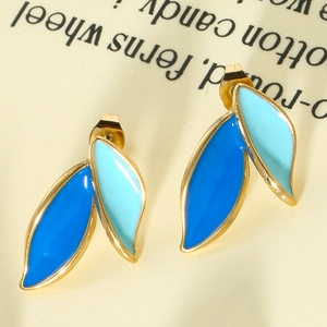 Macro shot of blue enamel leaf earrings with gold metal frame on a soft cream background