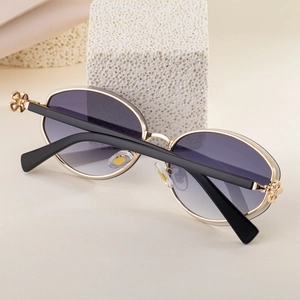 Detail of oval sunglasses with gold metal frame and hollow flower hinges on the temples