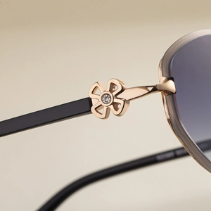 Detailed macro of oval sunglasses showing golden clover metal hinge and sparkling rhinestone