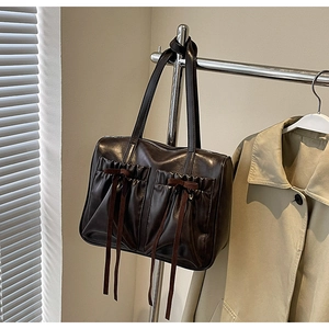 Detail of dark brown shoulder bag with pleated pockets and velvet bow accents