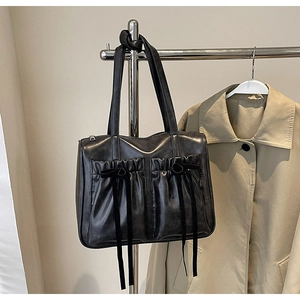 Detail of vintage black leather bag with ruffled pockets and ribbon bows on white wall