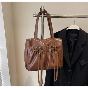 Detail of caramel brown retro shoulder bag featuring pleated pockets and bow accents