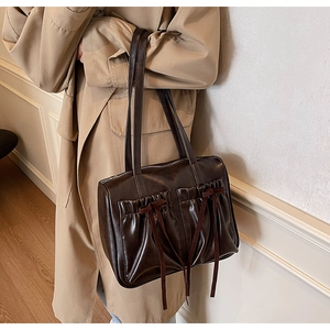 Detail of dark brown shoulder bag with bow ribbons and pleated pockets on trench coat